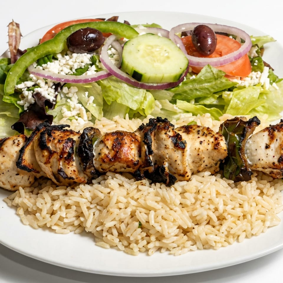Grilled chicken kebab with seasoned rice and Greek salad topped with cucumber, tomato, olives, red onion, and feta.